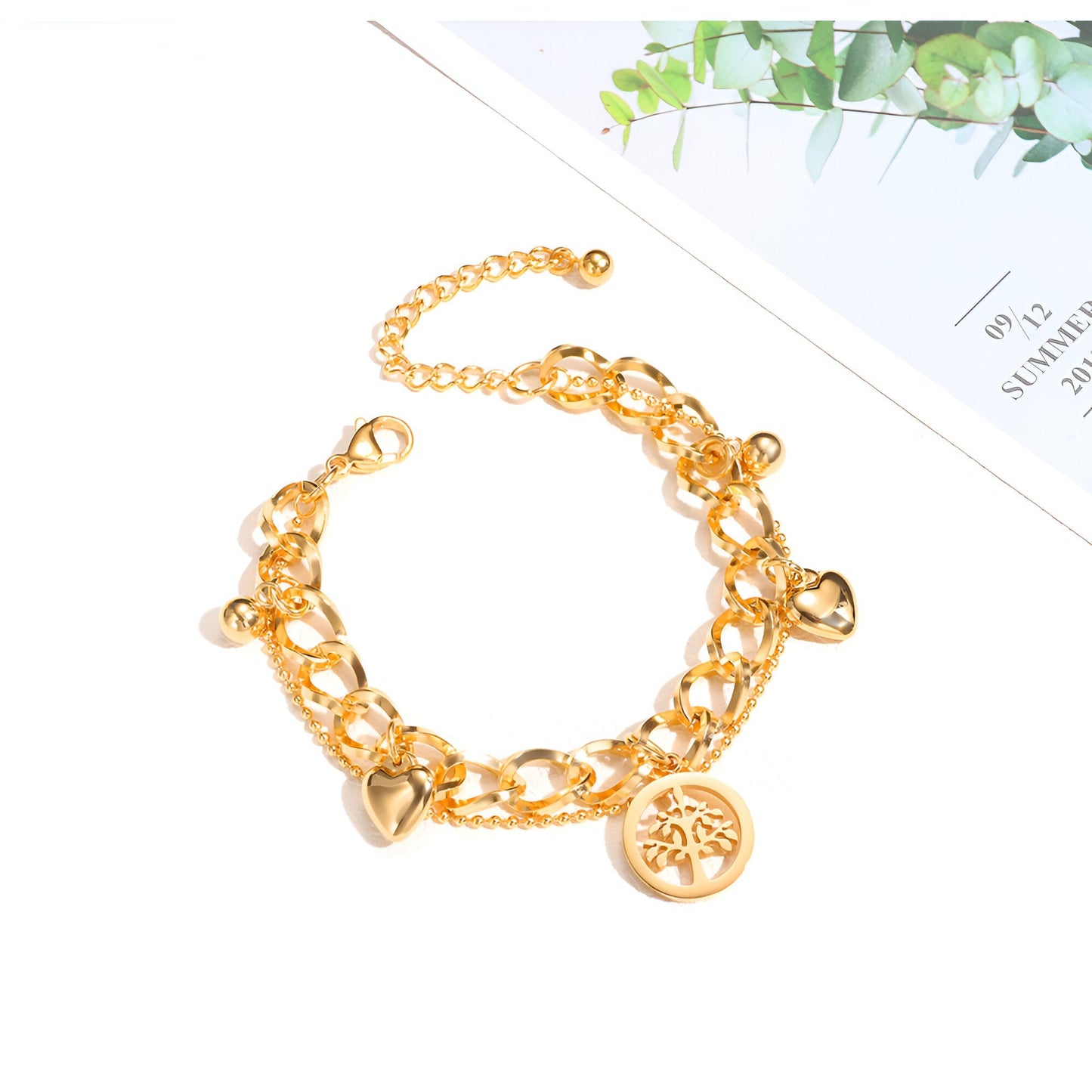 Bracelet doré en acier inoxydable avec maillons larges, pendentifs cœurs et arbre de vie finement gravé.